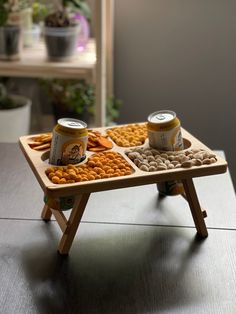 two cans of beer and some snacks on a wooden tray in front of a potted plant