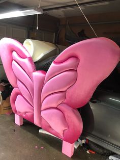 a pink butterfly shaped bench sitting next to a car