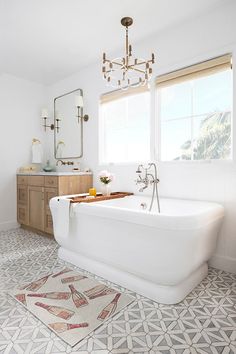 a white bath tub sitting under a window next to a sink in a bathroom on top of a tiled floor