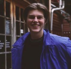 a young man is smiling in front of a metal caged area and wearing a blue jacket