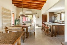 an open kitchen and dining room area with wood beams on the ceiling, white walls, and wooden furniture