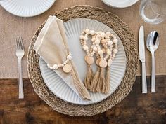 the table is set with white plates and silverware, napkins and wooden bead tassels