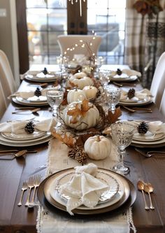 a dining room table set for thanksgiving with white pumpkins and pine cones on it