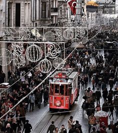 a crowd of people walking down a street next to a red trolley on the tracks