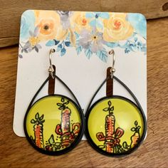 a pair of earrings with cactus designs hanging from it's earwires on top of a wooden table