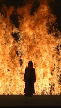 a person standing in front of a large fire with orange and yellow flames behind them