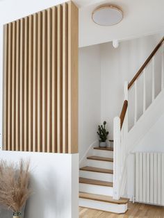 an empty room with white walls and wooden stairs, next to a potted plant