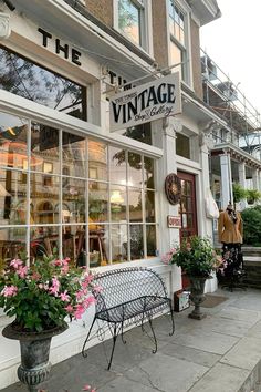 a store front with flowers in the window and an iron bench on the sidewalk outside