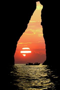 the sun is setting behind an arch in the water with boats on it and people paddling out