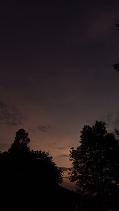 the sun is setting behind some trees in the dark sky with no one on it