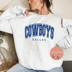 a woman wearing a sweatshirt with the word cowboys in blue on it, sitting next to a plant