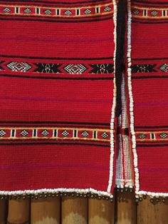 two pieces of red and black cloth with fringes on top of each other next to bamboo sticks