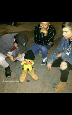 three young men sitting next to each other in front of a stuffed animal toy on the ground