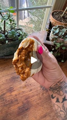 a hand holding a piece of food on top of a wooden table next to potted plants