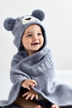 a baby wrapped in a bear towel on top of a white bed and smiling at the camera