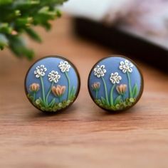 two blue and white flower studs sitting on top of a wooden table next to a plant