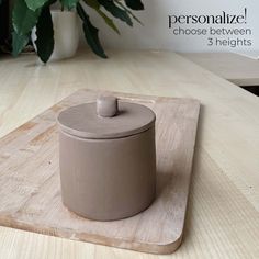 a wooden cutting board with a ceramic container on it and a potted plant in the background