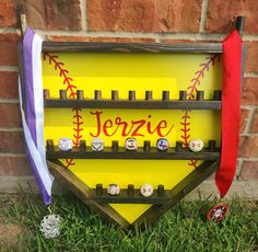 a wooden sign with baseballs and ribbons hanging from it's sides in front of a brick wall