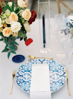 a blue and white plate with a menu sitting on top of it next to a vase filled with flowers