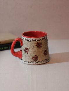 a red and white coffee cup sitting on top of a table next to a book