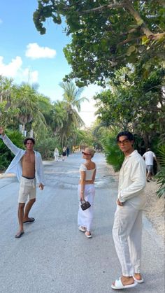 three people standing on the side of a road with palm trees in the back ground