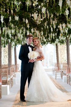 a bride and groom pose for a wedding photo in front of an archway decorated with flowers