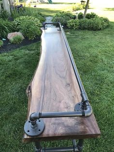 a long wooden table with metal pipes on it's sides and some grass in the background