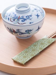 a bowl and chopsticks are sitting on a wooden tray next to a teapot