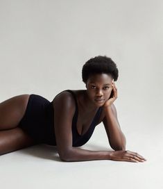 a woman laying on the ground in a black bodysuit with her hand under her chin