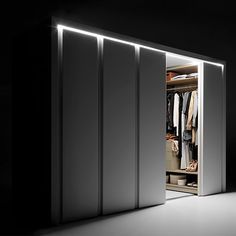 an open closet with clothes hanging on the shelves and lights shining down from above it