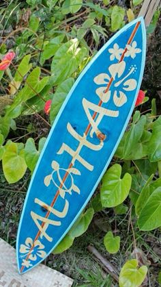 a blue surfboard sitting on the ground next to some green plants and red flowers