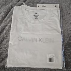 Size: Medium Color: White W/ Calvin Klein Across Chest. Calvin Klein Graphic Tee With Crew Neck, White Crew Neck Top By Calvin Klein, Calvin Klein Logo Print T-shirt For Spring, White Calvin Klein T-shirt For Spring, Calvin Klein Basic Short Sleeve Tops, White Calvin Klein Crew Neck Top, Calvin Klein Graphic Tee For Streetwear, Calvin Klein White Crew Neck Top, Sporty Calvin Klein Tops With Logo Print