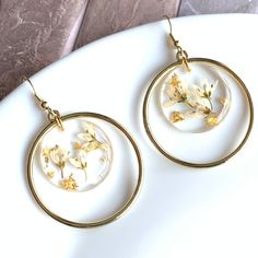 a pair of gold hoop earrings with pressed flowers in them on a white plate against a marble background