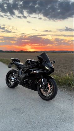 a black motorcycle parked on the side of a road next to a grass covered field