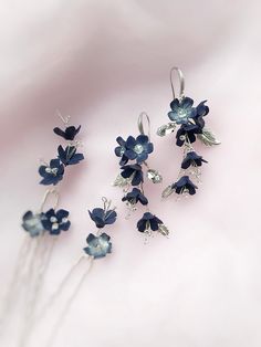 five blue flowers are attached to silver hair pins on a white surface with pink background