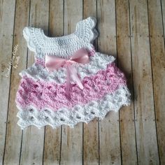 a pink and white crocheted dress laying on top of a wooden floor