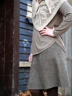 a woman standing in front of a blue building wearing a sweater and skirt with a scarf around her neck