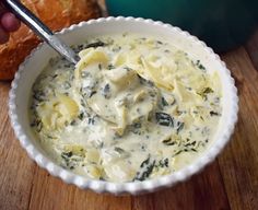 a white bowl filled with cheese and spinach sauce on top of a wooden table