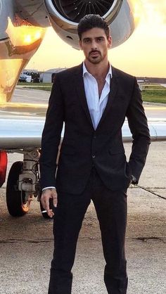 a man standing in front of an airplane with his hand on his hip and looking at the camera