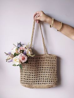 a hand holding a straw bag with flowers in it on a white wall next to a person's arm