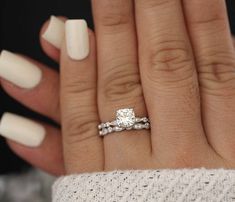 a woman's hand with white nails and a ring on her finger, holding a diamond