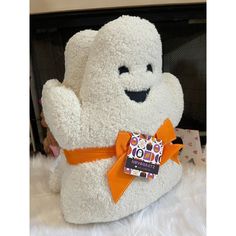 a white teddy bear with an orange ribbon around it's neck sitting on a fluffy surface