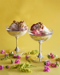 two glasses filled with ice cream sitting on top of a yellow table next to pink flowers