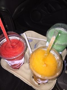 three different colored drinks sitting on top of a tray in the back seat of a car