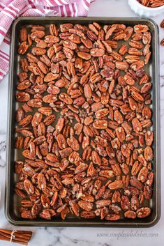 pecans in a baking pan on a marble counter top with cinnamon sticks and napkins