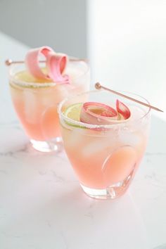 two glasses filled with drinks sitting on top of a white counter next to each other