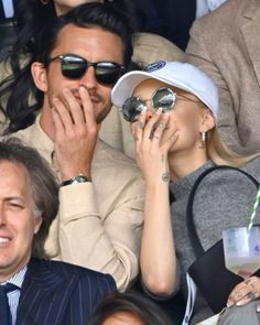 a man and woman sitting next to each other at a tennis game with their hands covering their faces