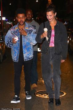 a man and woman walking down the street at night holding ice cream cones in their hands