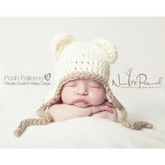 a baby wearing a knitted bear hat sleeping on top of a white blanket with his hands under his chin