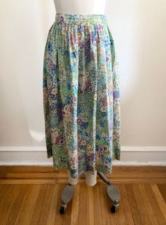 "Bright blue multicolored floral print midi-skirt, from the 1980s. Waist measures 14\" (36 cm) flat across and hip measures 22.5\" (57 cm) flat across. The skirt is 31\" (79 cm) long. The original size is a US 10. 100% polyester." Floral Print Full Skirt For Daywear, Floral Print Relaxed Fit Skirt For Daywear, Relaxed Multicolor Floral Print Skirt, Multicolor Floral Print Skirt For Garden Party, Retro Blue Floral Print Skirt, Blue Retro Skirt With Floral Print, Vintage Floral Print Bottoms For Spring, Vintage Lined Skirt For Spring, Vintage Green Tiered Skirt